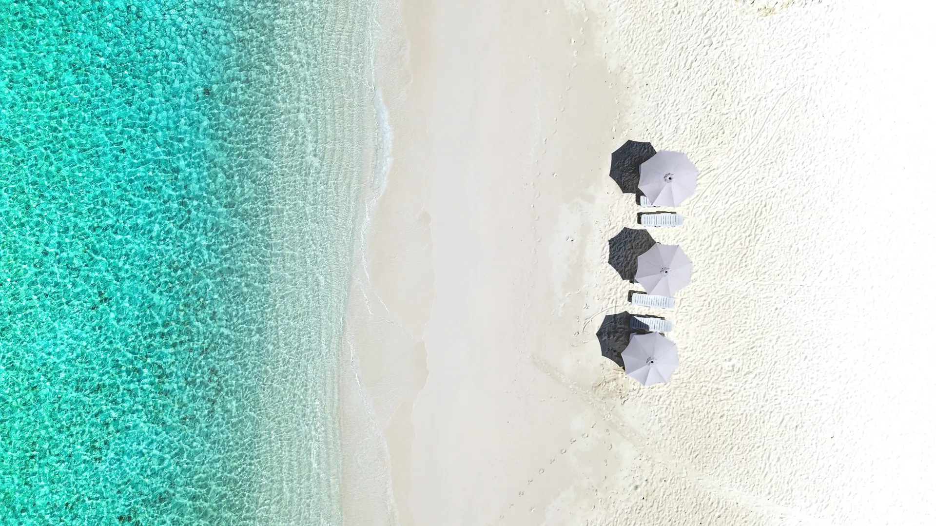 Beach umbrellas on white sand beside the lagoon, seen from above